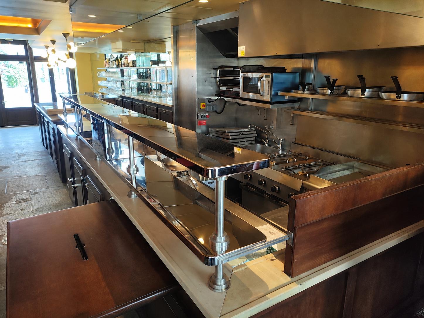 Agencement inox sur mesure dans une cuisine professionnelle de restaurant avec ligne de cuisson, passe-plat et équipements inox fabriqués par Paris Inox