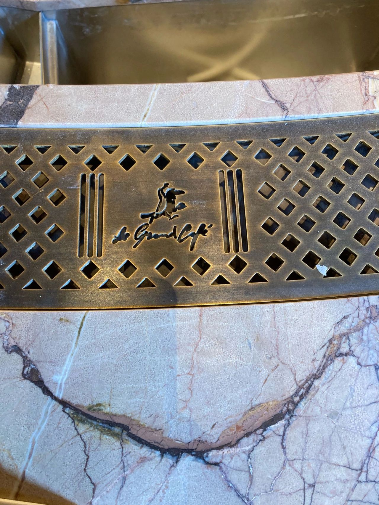 Grille inox personnalisée intégrée au bar du Grand Café Détail d'une grille inox découpée au laser avec logo Le Grand Café intégrée dans un bar sur mesure réalisé par Paris Inox.