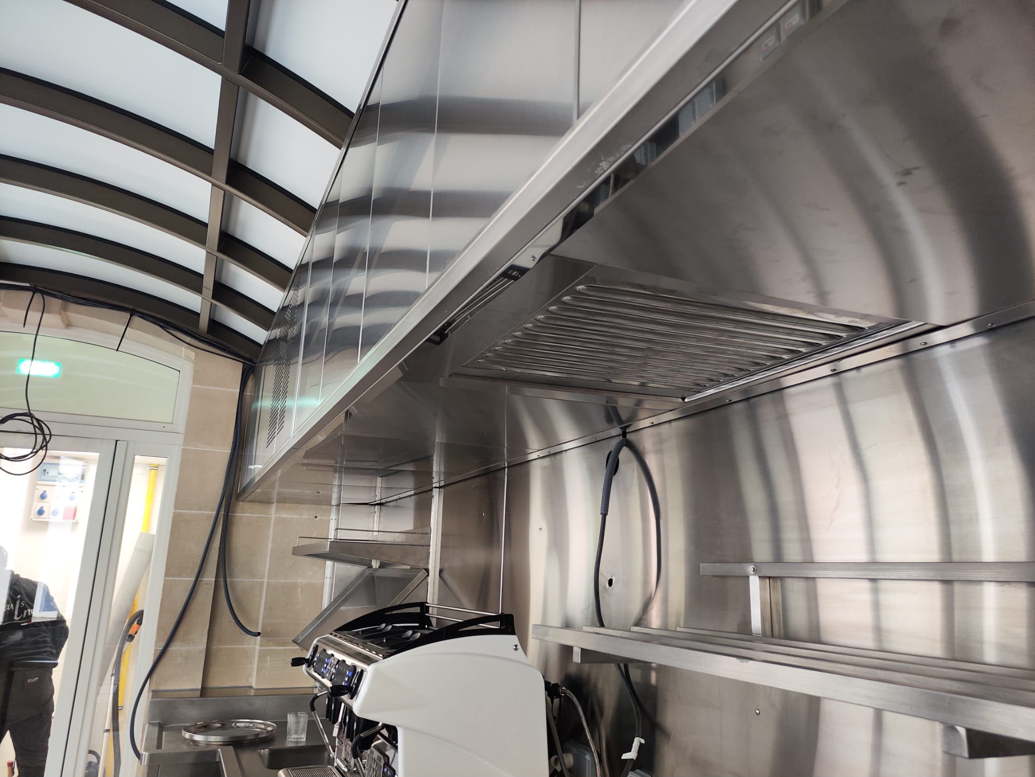 Aménagement inox sur mesure pour espace professionnel Ensemble inox professionnel sur mesure avec plan de travail, évier intégré, étagères murales et habillage inox destiné à un espace café et restauration.