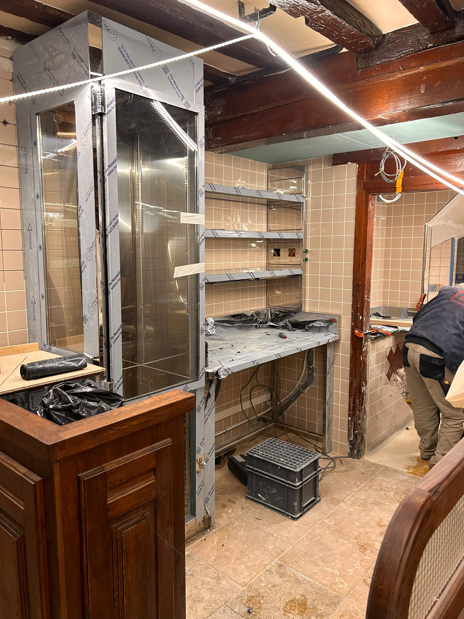 Installation d’un arrière-bar inox sur mesure Arrière-bar inox sur mesure en cours d'installation avec cave réfrigérée, étagères murales et plan de travail professionnel.