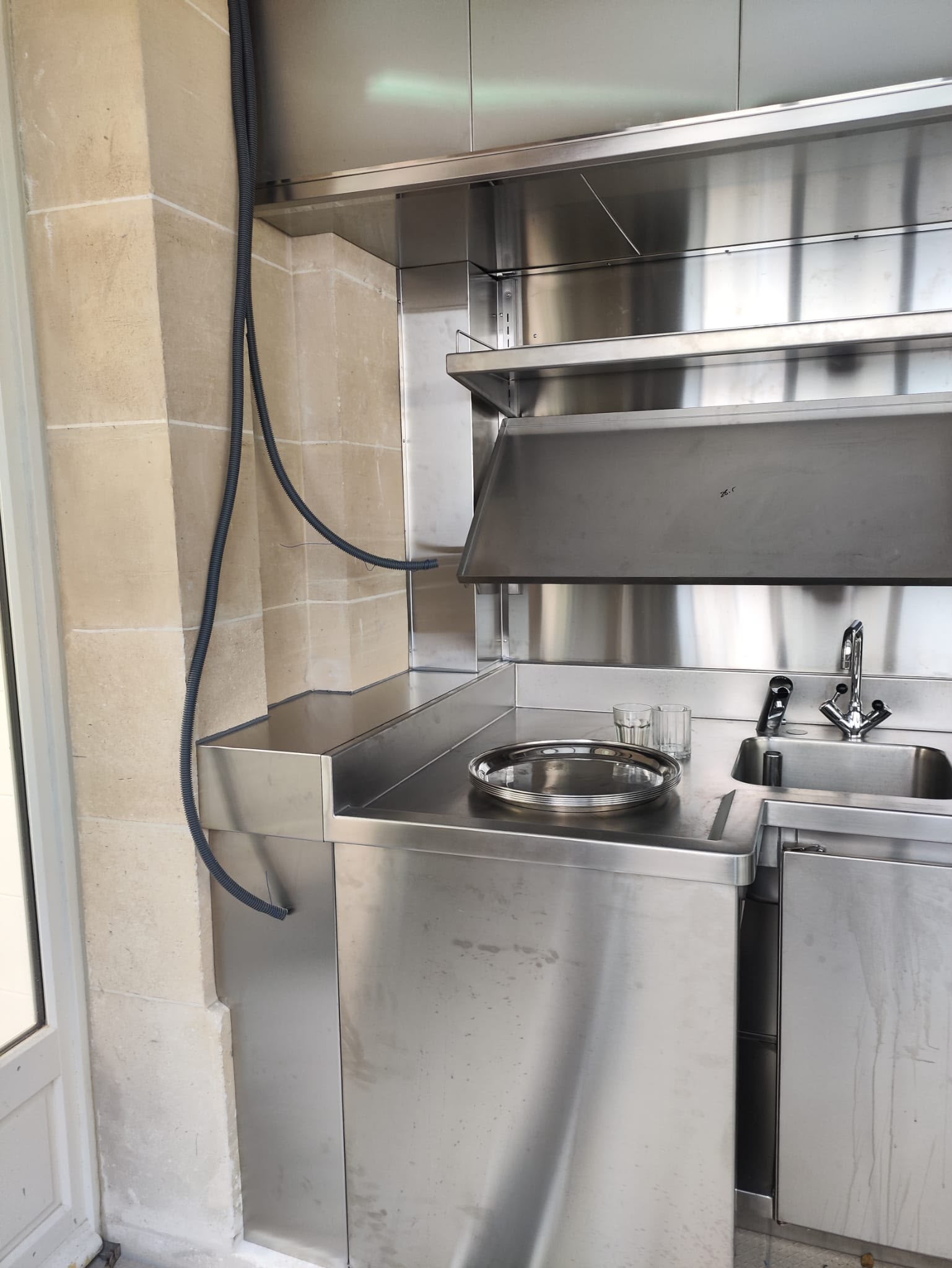 Poste café professionnel en inox sur mesure Poste café professionnel en inox fabriqué sur mesure avec plan de travail, évier intégré, crédence inox et étagères murales pour établissement de restauration.